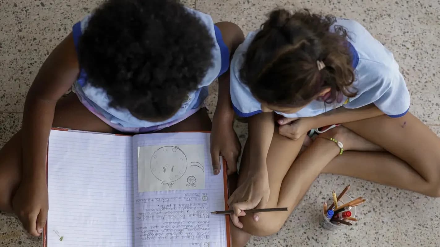 Crianças desenham e escrevem em escola pública, tema ligado às políticas de direitos humanos de Lula e Flávio