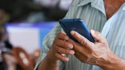 Homem segura celular nas mãos, em foco em close nos dedos e no aparelho