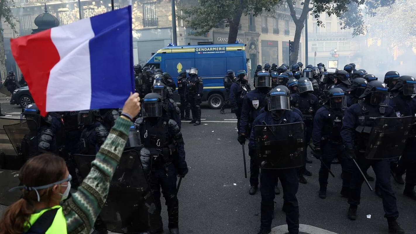 Manifestante segura bandeira da França em frente a policiais durante protesto em Paris