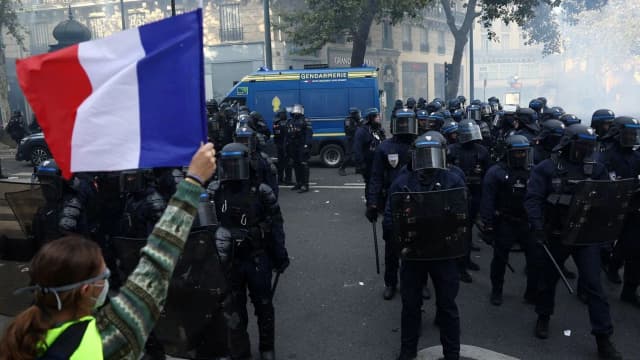 Manifestante segura bandeira da França em frente a policiais durante protesto em Paris