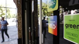 Pessoa caminha em frente a comércio com adesivos de vale-alimentação e cartões de pagamento, foto de arquivo sobre consumo no Brasil