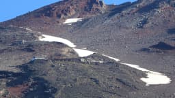 Encosta rochosa do Monte Fuji na trilha Fujinomiya, com refúgios de montanha e faixas de neve remanescente