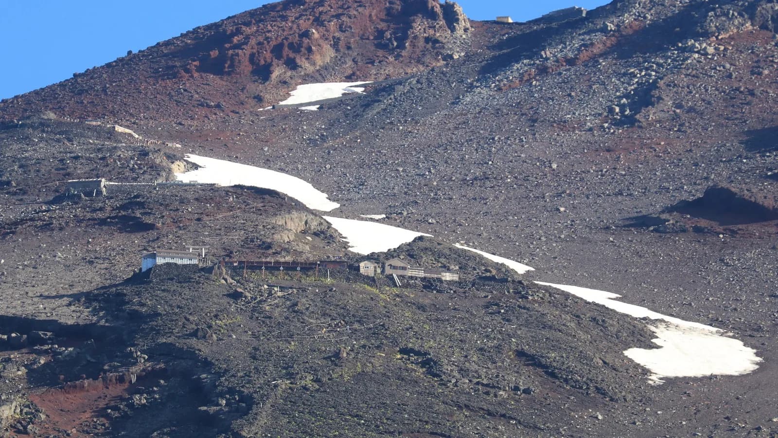 Encosta rochosa do Monte Fuji na trilha Fujinomiya, com refúgios de montanha e faixas de neve remanescente