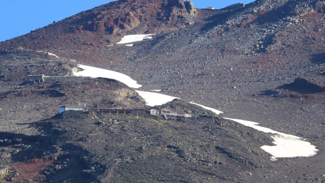 Encosta rochosa do Monte Fuji na trilha Fujinomiya, com refúgios de montanha e faixas de neve remanescente