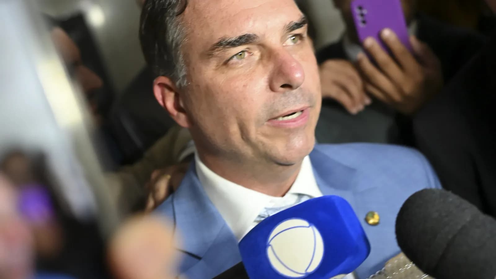 Senador Flávio Bolsonaro fala a jornalistas cercado de microfones e celulares