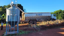 Caminhão de nutrição animal descarrega ração em silo vertical numa propriedade rural, com dois trabalhadores no local