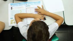 Estudante em sala de aula, com material escolar sobre a mesa