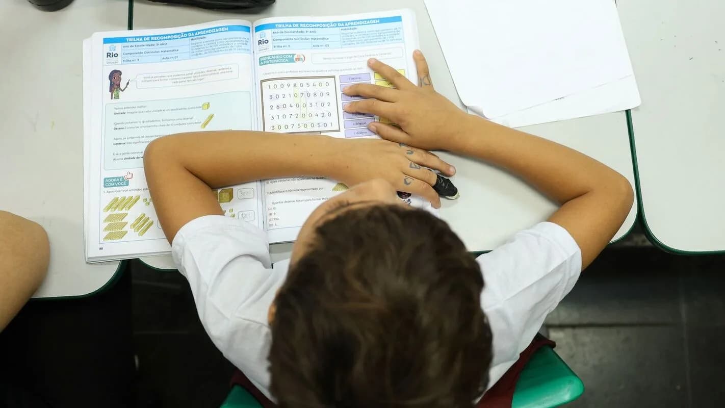 Estudante em sala de aula, com material escolar sobre a mesa