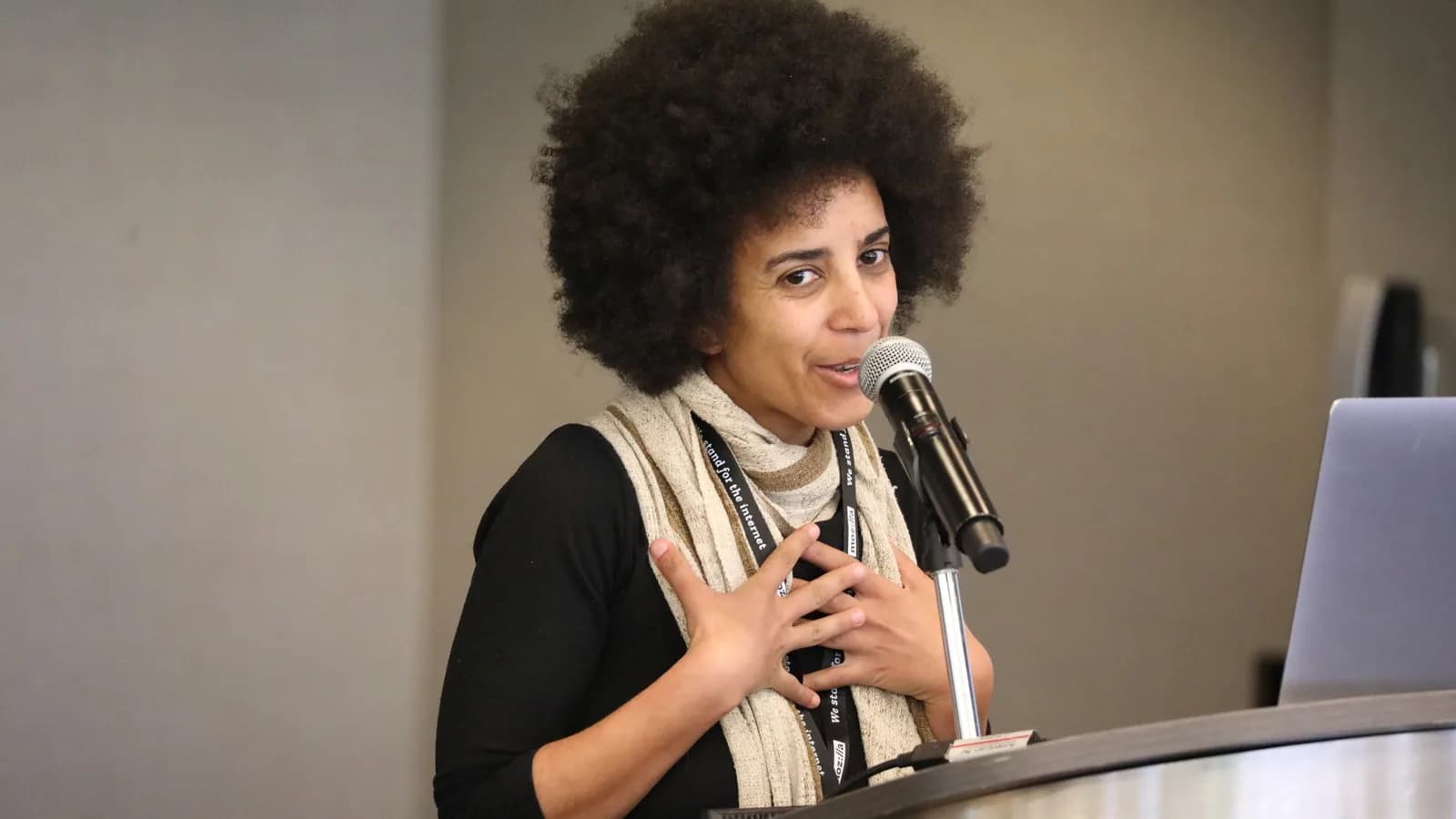 Timnit Gebru discursa em conferência, com laptop e microfone à sua frente
