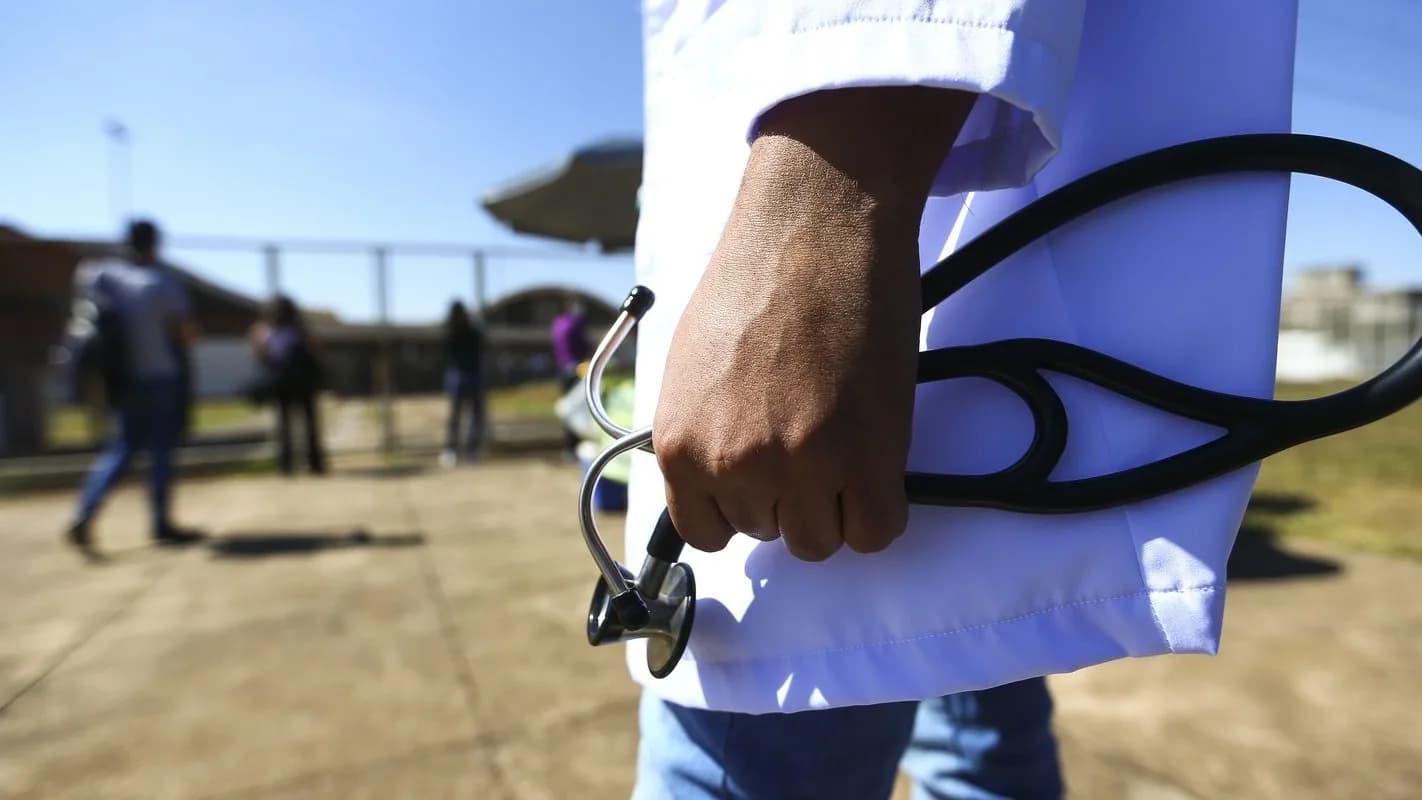 Mão de pessoa vestindo jaleco branco segura estetoscópio, em foto de arquivo ilustrando o setor de ensino médico no Brasil