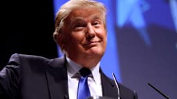 Donald Trump discursa em evento político, de terno escuro e gravata azul