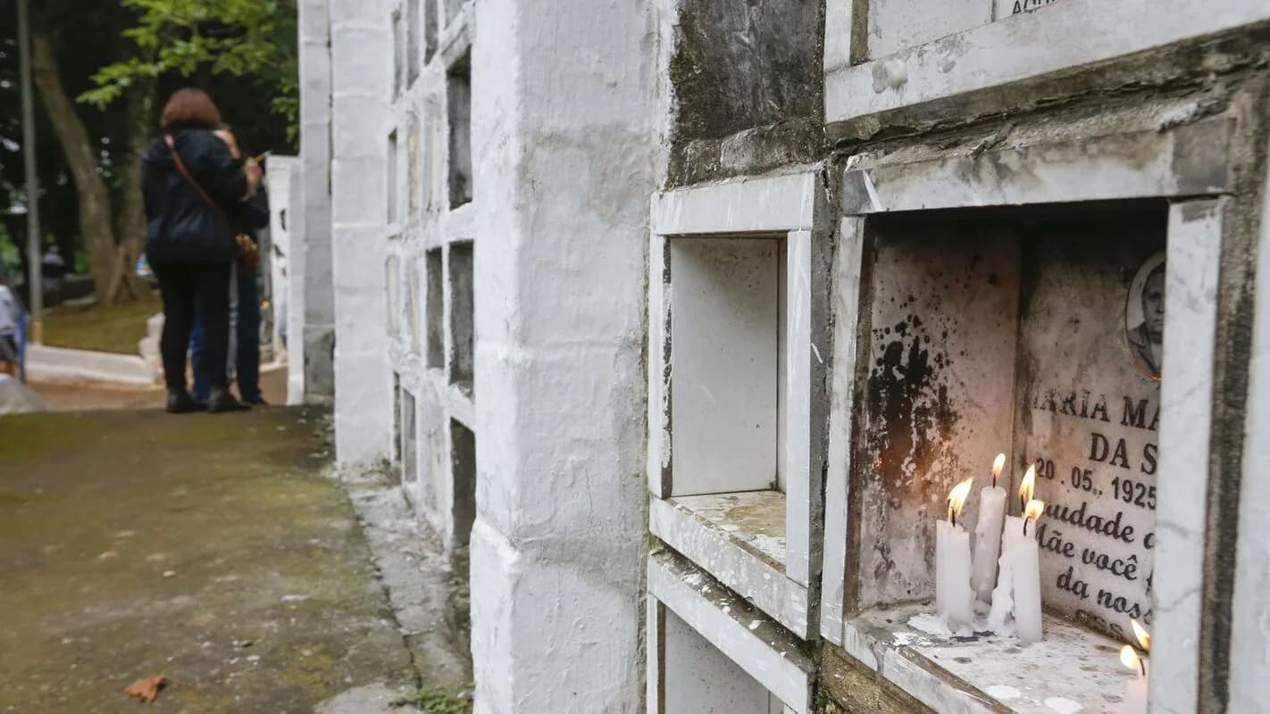 Pessoas em frente a gavetas de um cemitério em São Paulo, com velas acesas em memória de um ente querido