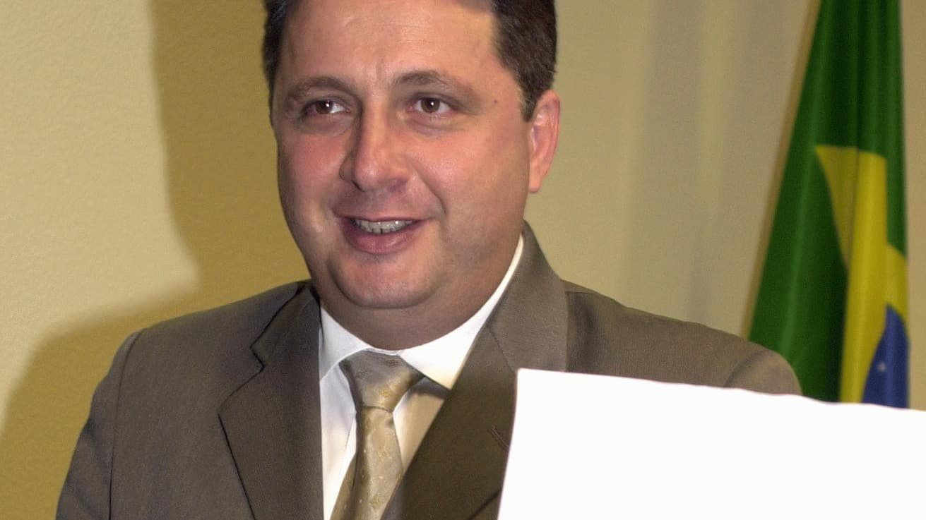 O ex-governador Anthony Garotinho sorri ao apresentar um documento, com a bandeira do Brasil ao fundo, em foto de arquivo