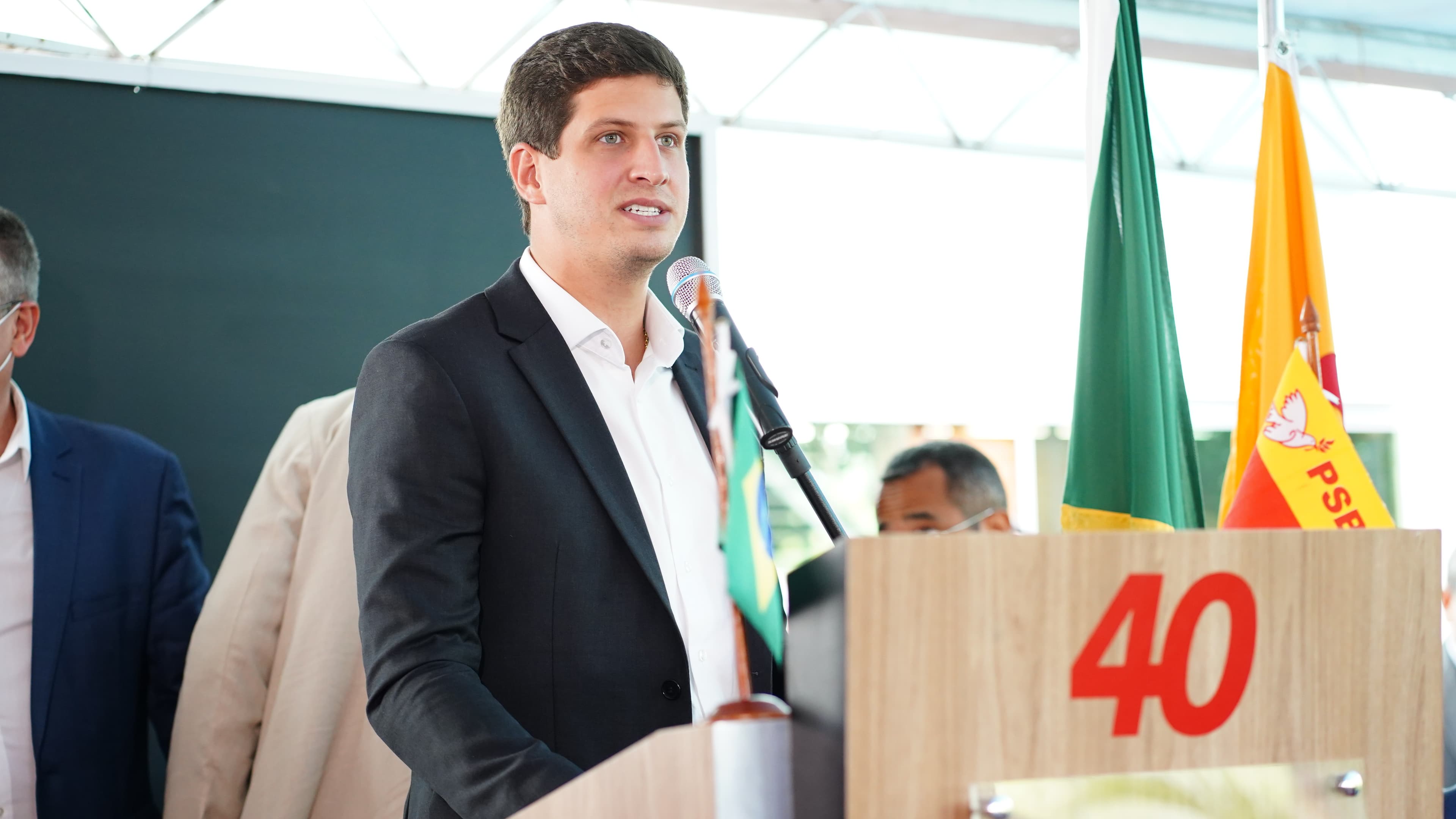 João Campos discursa em púlpito com bandeiras do Brasil e do PSB ao fundo, em foto de arquivo de evento do partido