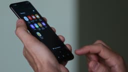 Mãos de uma pessoa segurando e mexendo em um smartphone Android com tela de aplicativos acesa