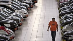 Consumidor caminha entre fileiras de carros em pátio de revendedora de veículos
