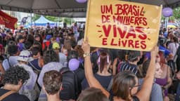 Imagem de arquivo de ato contra o feminicídio em Brasília: multidão em manifestação e, em primeiro plano, cartaz com os dizeres 'Um Brasil de mulheres vivas e livres'