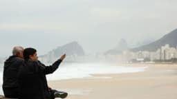 Casal agasalhado observa o mar em dia frio e nublado em Copacabana, no Rio de Janeiro