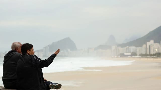 Casal agasalhado observa o mar em dia frio e nublado em Copacabana, no Rio de Janeiro