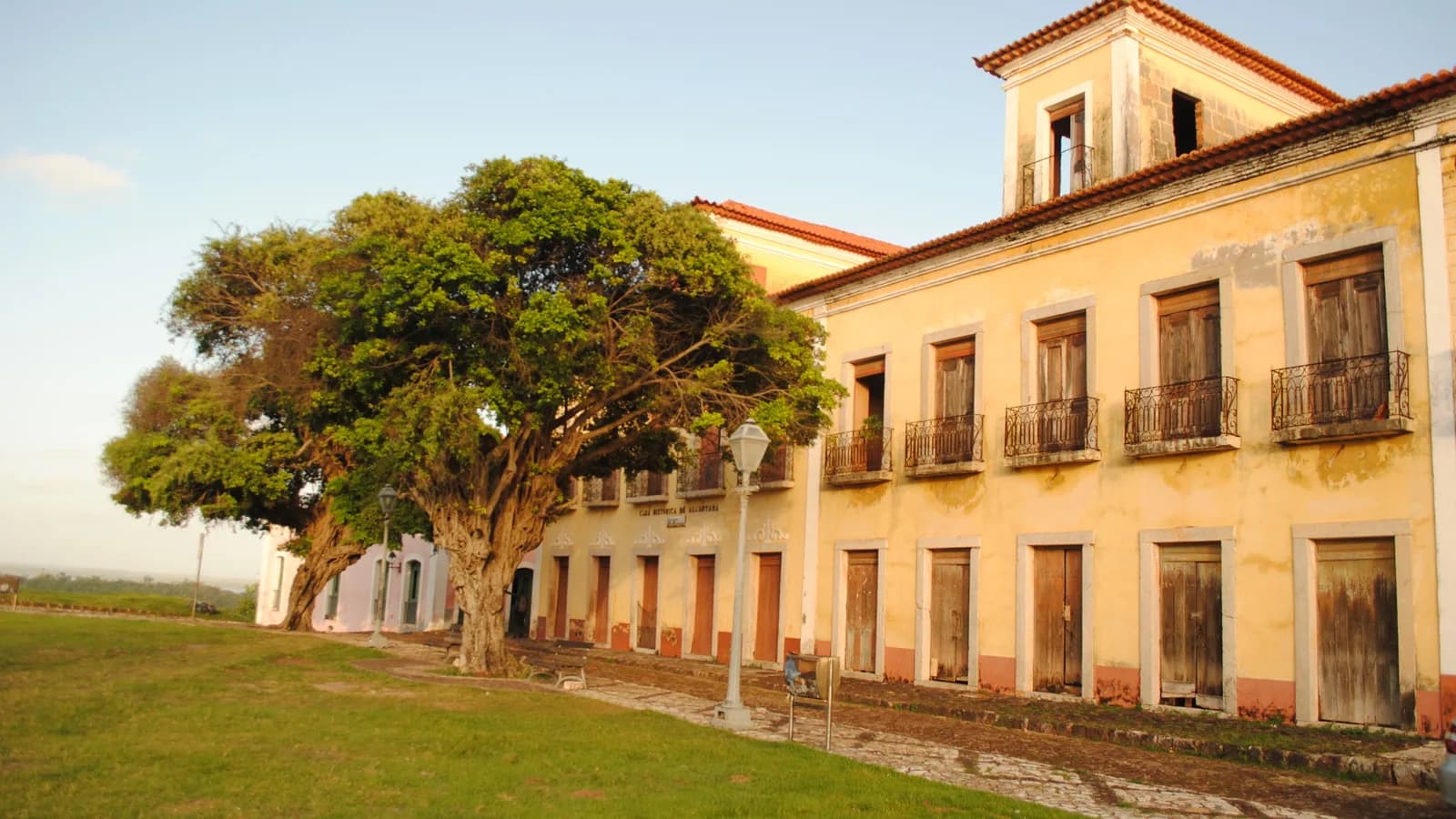 Fachada de casarão colonial amarelo com sacadas de ferro em Alcântara, Maranhão, ao lado de uma árvore frondosa