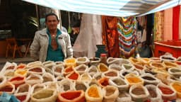 Feirante organiza sacos coloridos de temperos e especiarias em barraca de feira
