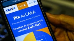 Mão segura celular com a tela do aplicativo do Pix na Caixa, sistema de pagamento instantâneo brasileiro
