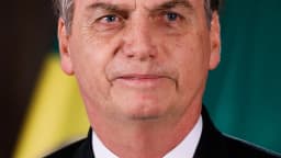 Jair Bolsonaro em retrato oficial, de terno escuro, com bandeiras do Brasil ao fundo