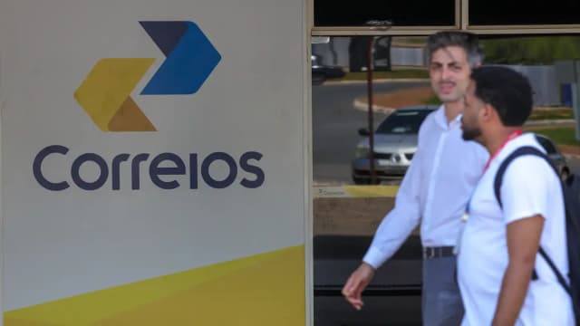 Fachada com logo dos Correios e pedestres passando em frente a uma agência, foto de arquivo
