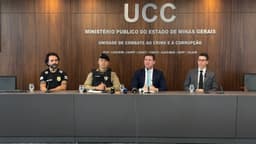 Delegado, capitão da PM e dois promotores do MPMG sentados em coletiva de imprensa, com painel da Unidade de Combate ao Crime e à Corrupção ao fundo