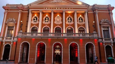 Fachada iluminada do Theatro da Paz, em Belém, com colunas, arcos e o nome do teatro no alto do frontão ao entardecer