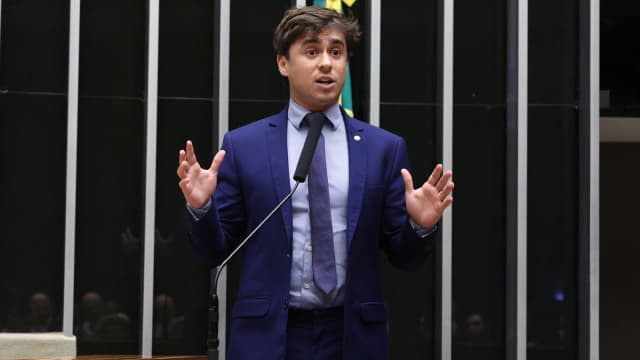 O deputado Nikolas Ferreira discursa com as mãos levantadas na tribuna da Câmara dos Deputados