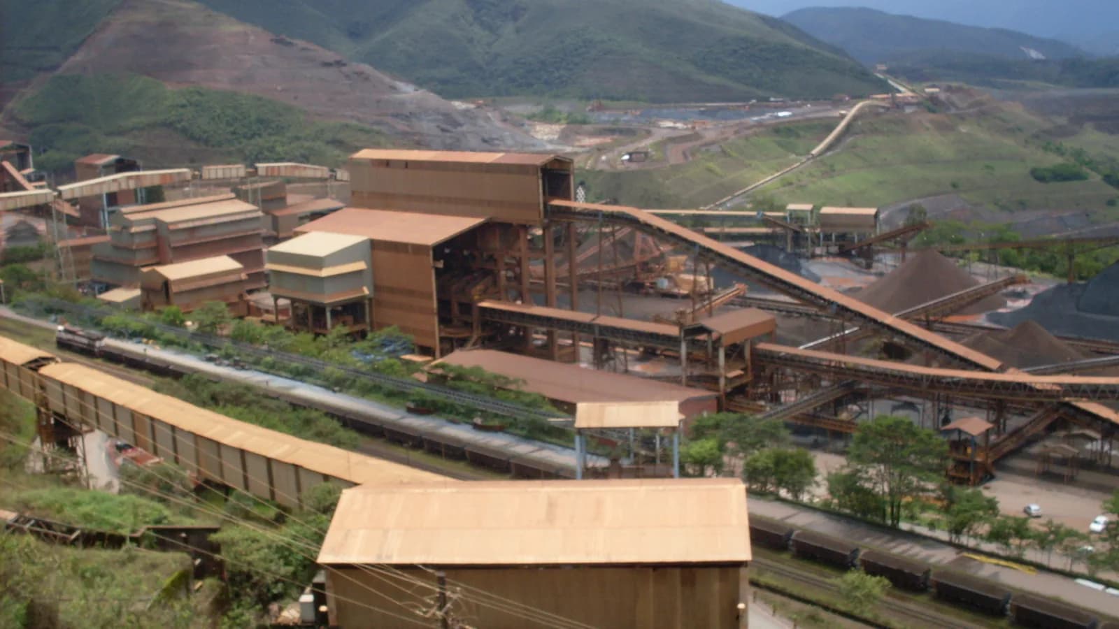 Complexo industrial de mineração de minério de ferro da Vale, com esteiras, vagões e pátio de estocagem entre montanhas, em Minas Gerais