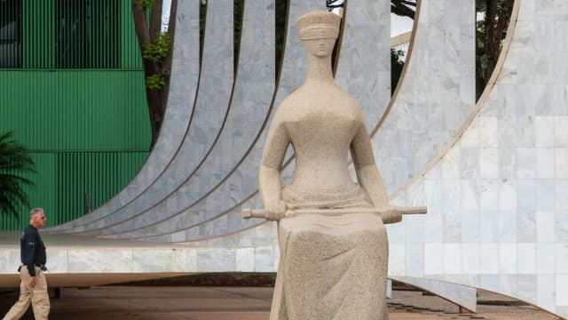 Estátua da Justiça em frente ao STF, em Brasília, com agente de segurança passando ao lado