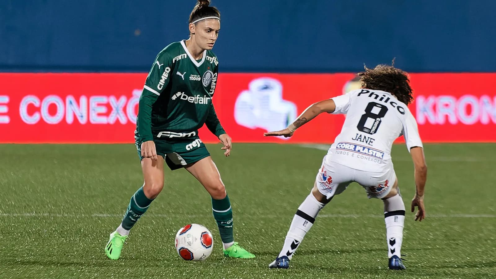 Jogadora do Palmeiras de uniforme verde disputa a bola com jogadora do Santos durante partida de futebol feminino