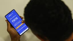 Trabalhador de costas segura um celular com a tela inicial do aplicativo do FGTS aberta