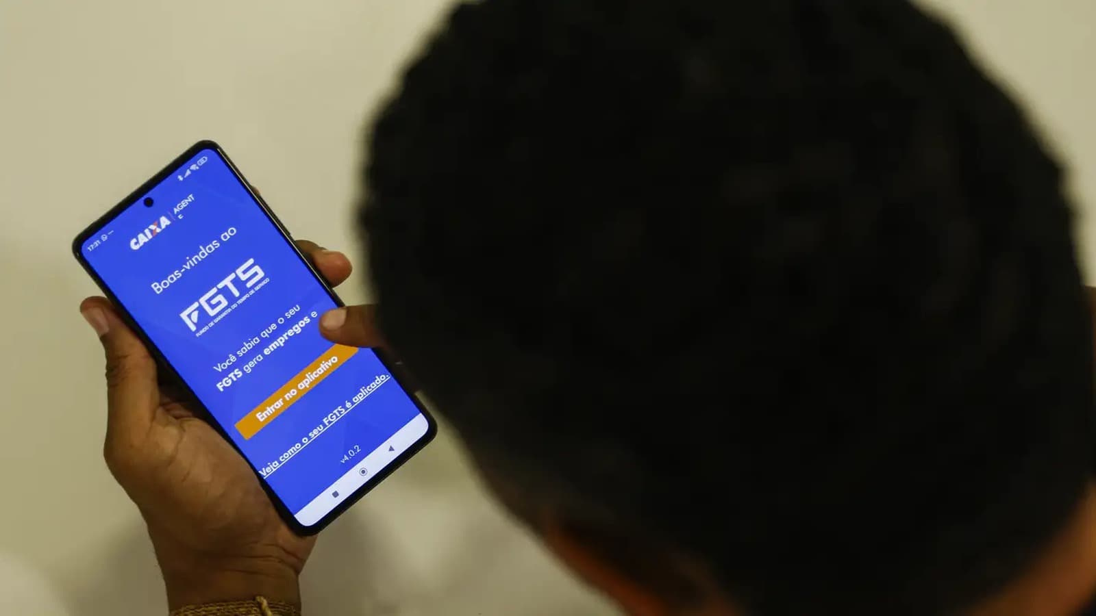 Trabalhador de costas segura um celular com a tela inicial do aplicativo do FGTS aberta