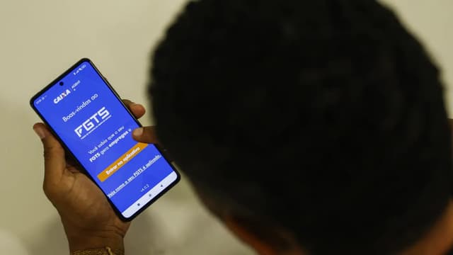 Trabalhador de costas segura um celular com a tela inicial do aplicativo do FGTS aberta