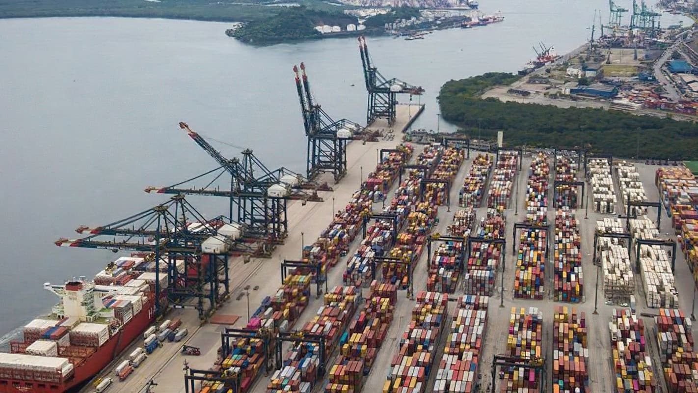 Vista aérea do Porto de Santos com navio cargueiro atracado, guindastes e pátio de contêineres