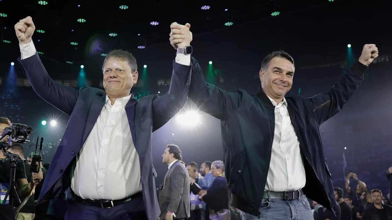 Tarcísio de Freitas e Flávio Bolsonaro de mãos dadas erguidas em evento de campanha