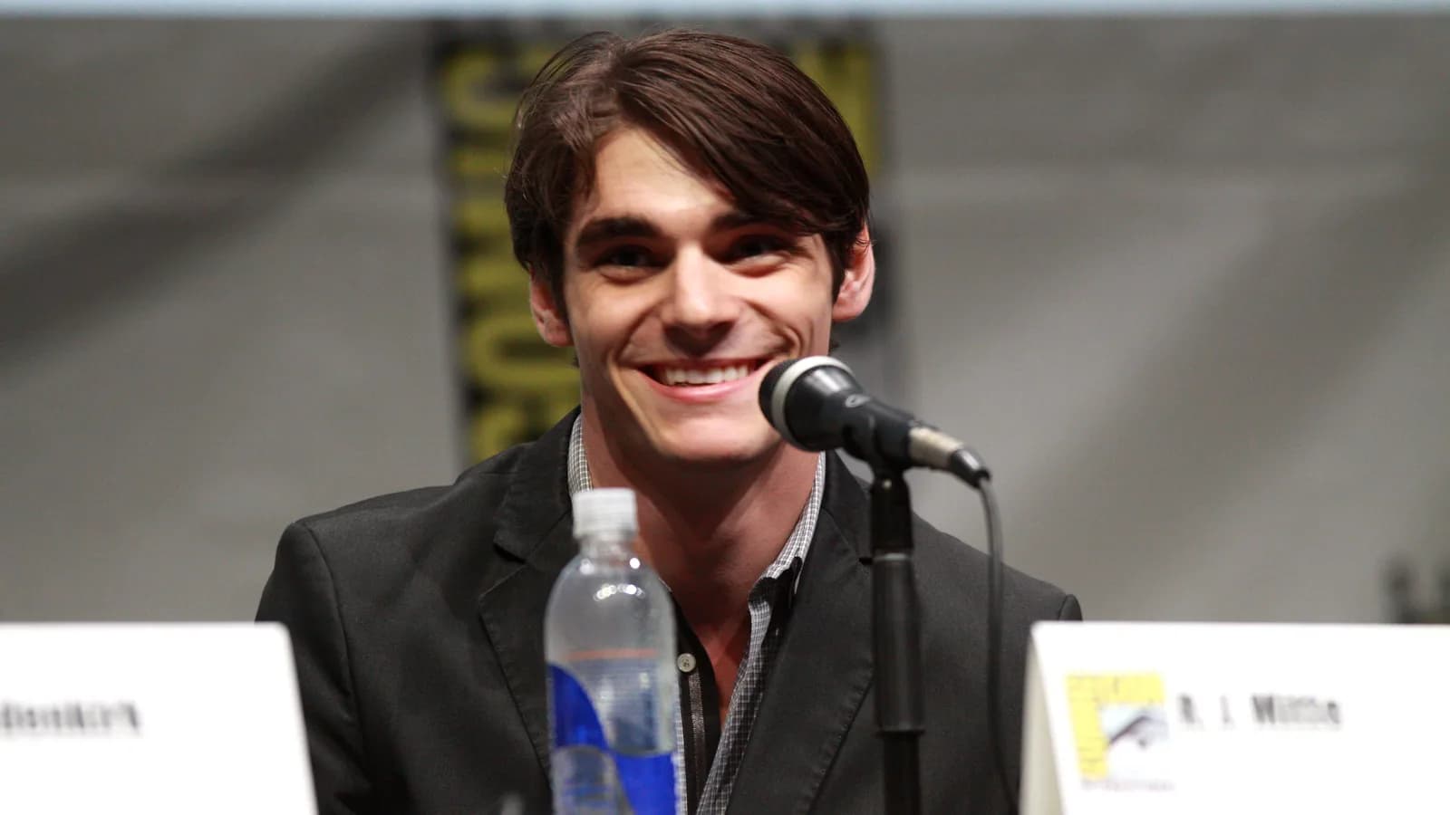 RJ Mitte em painel de convenção, sorrindo ao microfone