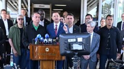 Jair Bolsonaro, de camisa verde, e o senador Flávio Bolsonaro atrás de um púlpito do Senado Federal durante entrevista coletiva, cercados por parlamentares e microfones da imprensa, em imagem de arquivo de julho de 2025