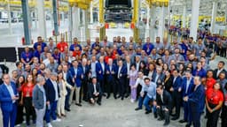 O presidente Lula, cercado por dezenas de trabalhadores brasileiros e executivos chineses, faz sinal de positivo na linha de montagem da fábrica da BYD em Camaçari, com um veículo suspenso ao fundo