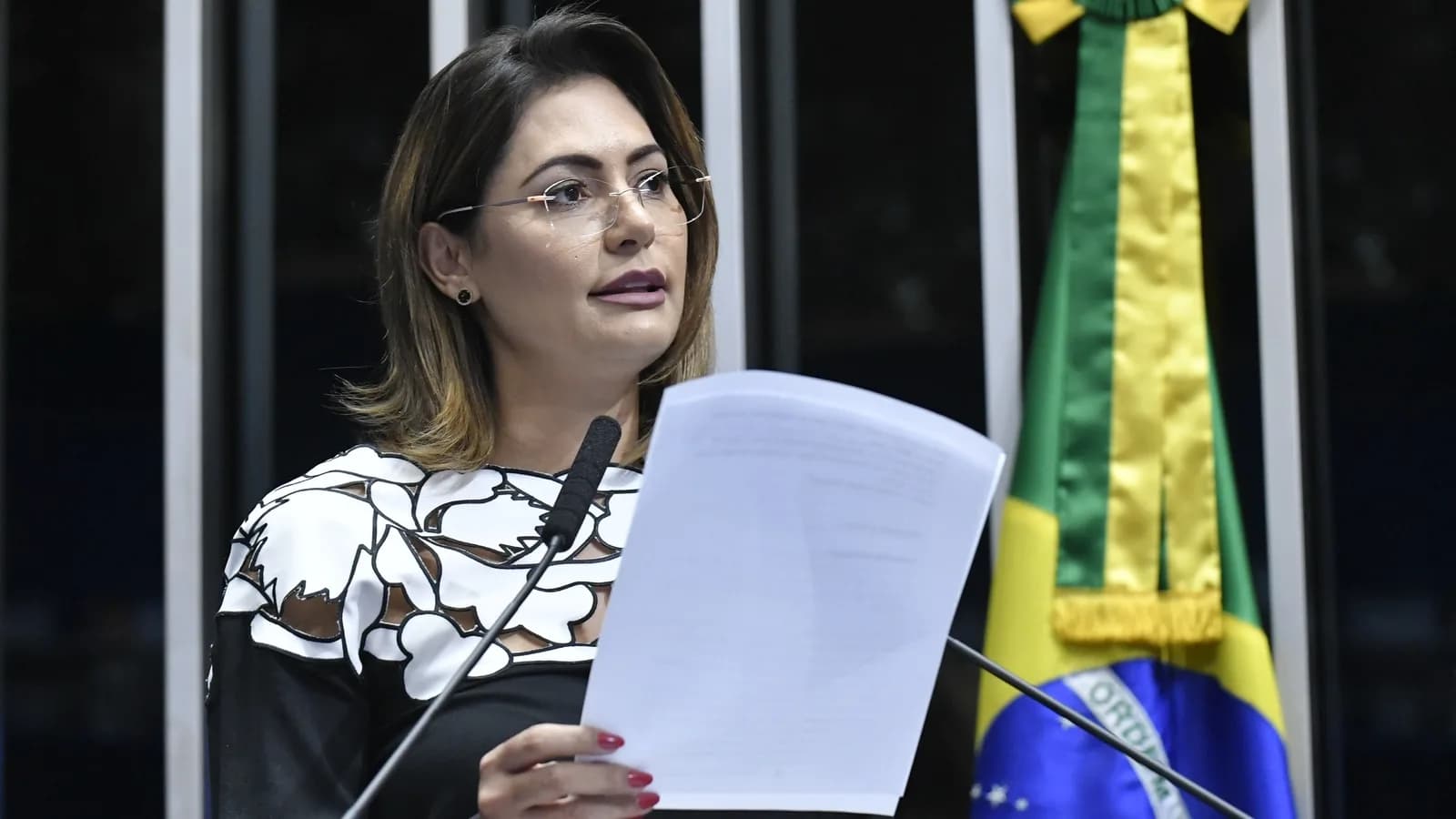 Michelle Bolsonaro discursa em púlpito do Senado com bandeira do Brasil ao fundo