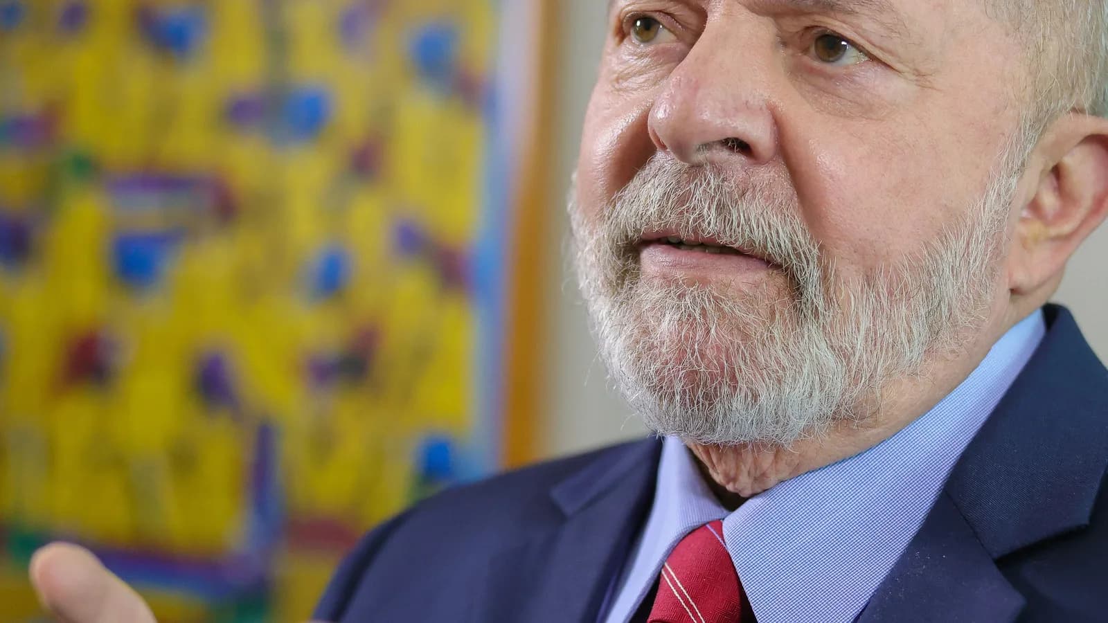Presidente Luiz Inácio Lula da Silva gesticula durante entrevista, vestindo terno azul e gravata vermelha