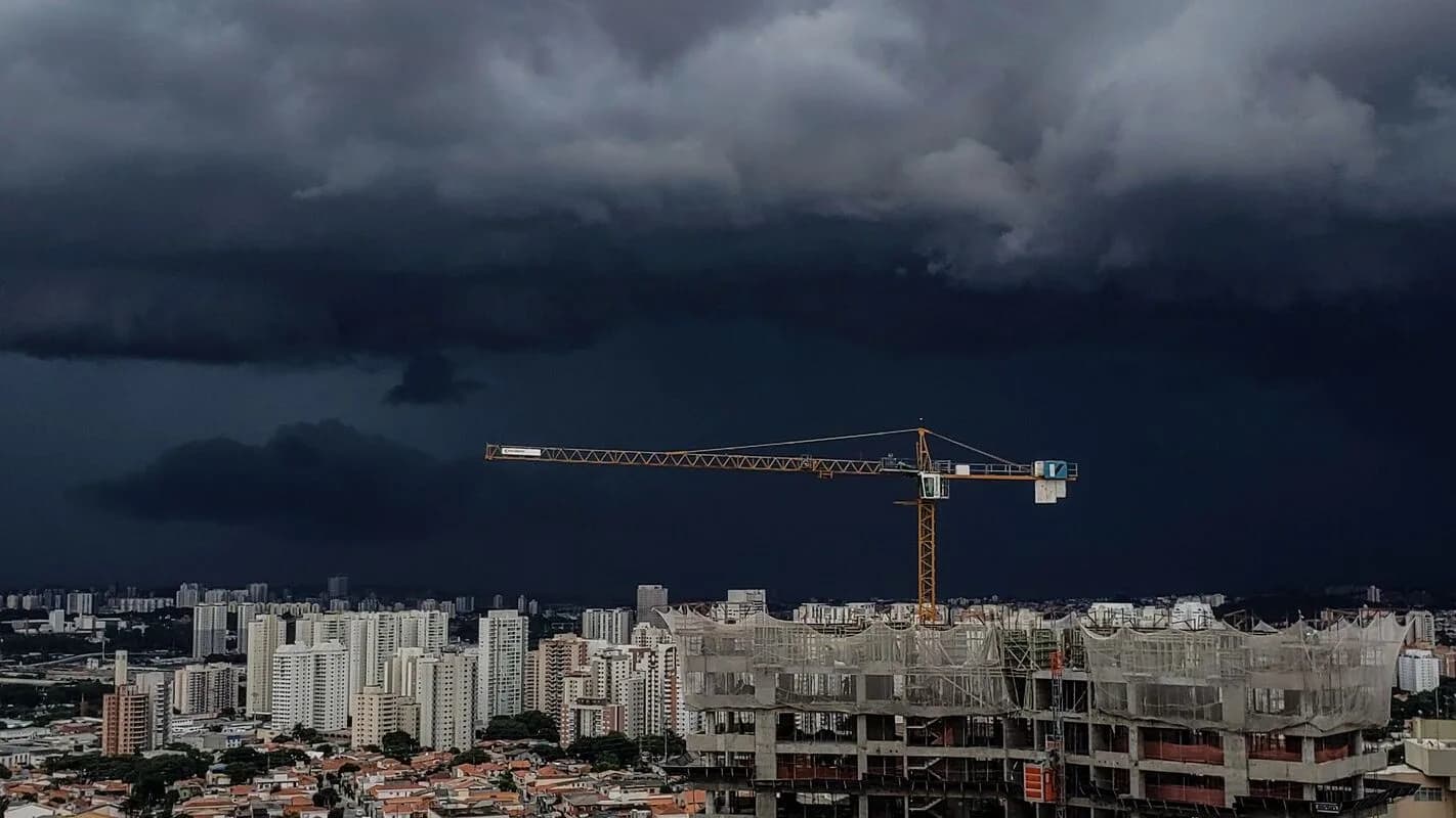 Céu com nuvens escuras de tempestade sobre área urbana, com guindaste de obra ao fundo