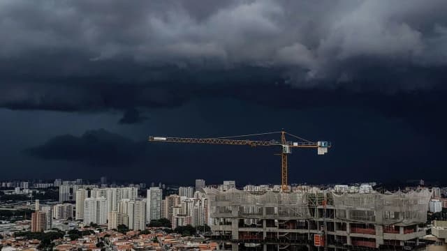 Céu com nuvens escuras de tempestade sobre área urbana, com guindaste de obra ao fundo