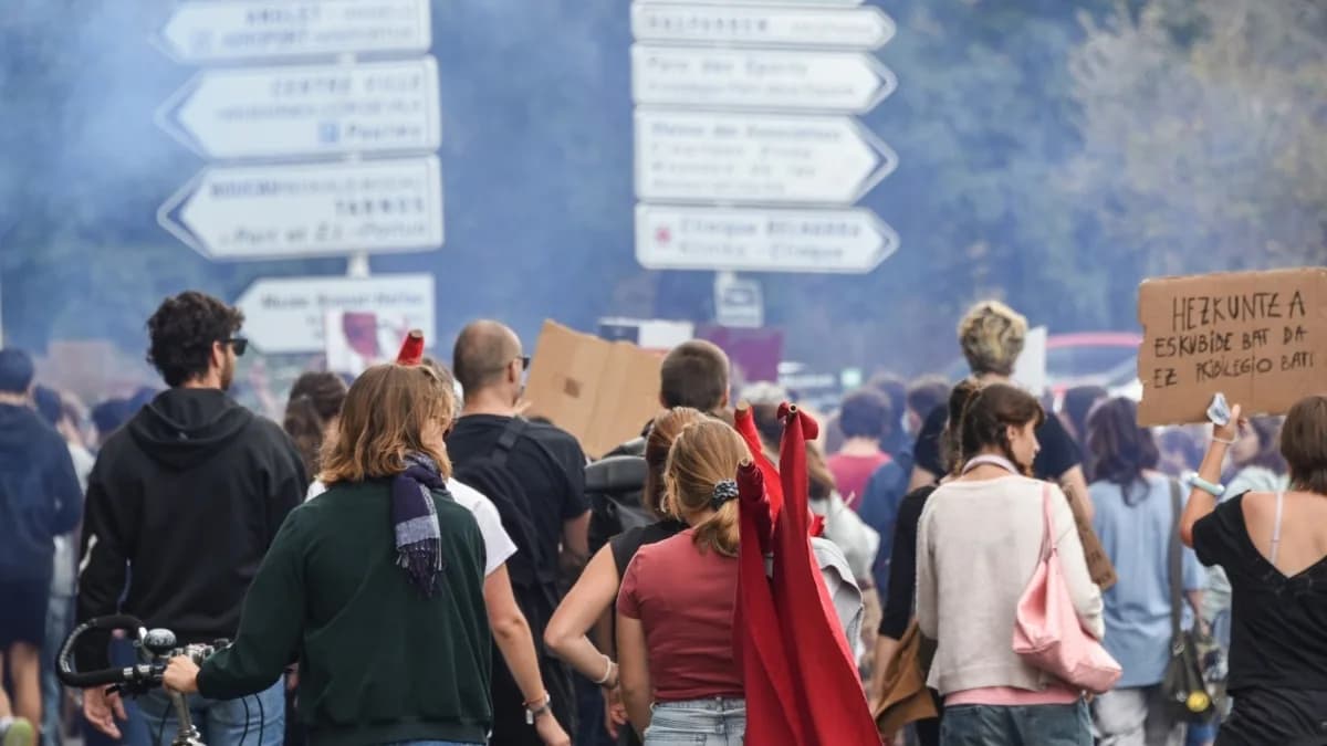 Manifestantes de costas em protesto estudantil nas ruas de Bayonne, na França, com fumaça ao fundo