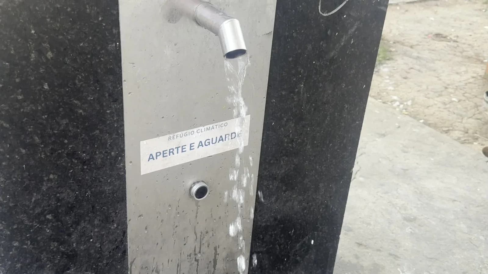 Água sai da bica do bebedouro do refúgio climático da Avenida Olegário Maciel, no Centro de Belo Horizonte, acima da placa "Aperte e aguarde"