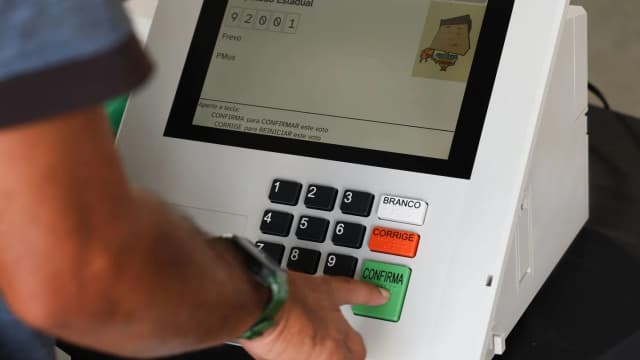Mão de eleitor pressiona o botão de confirmação em urna eletrônica durante votação