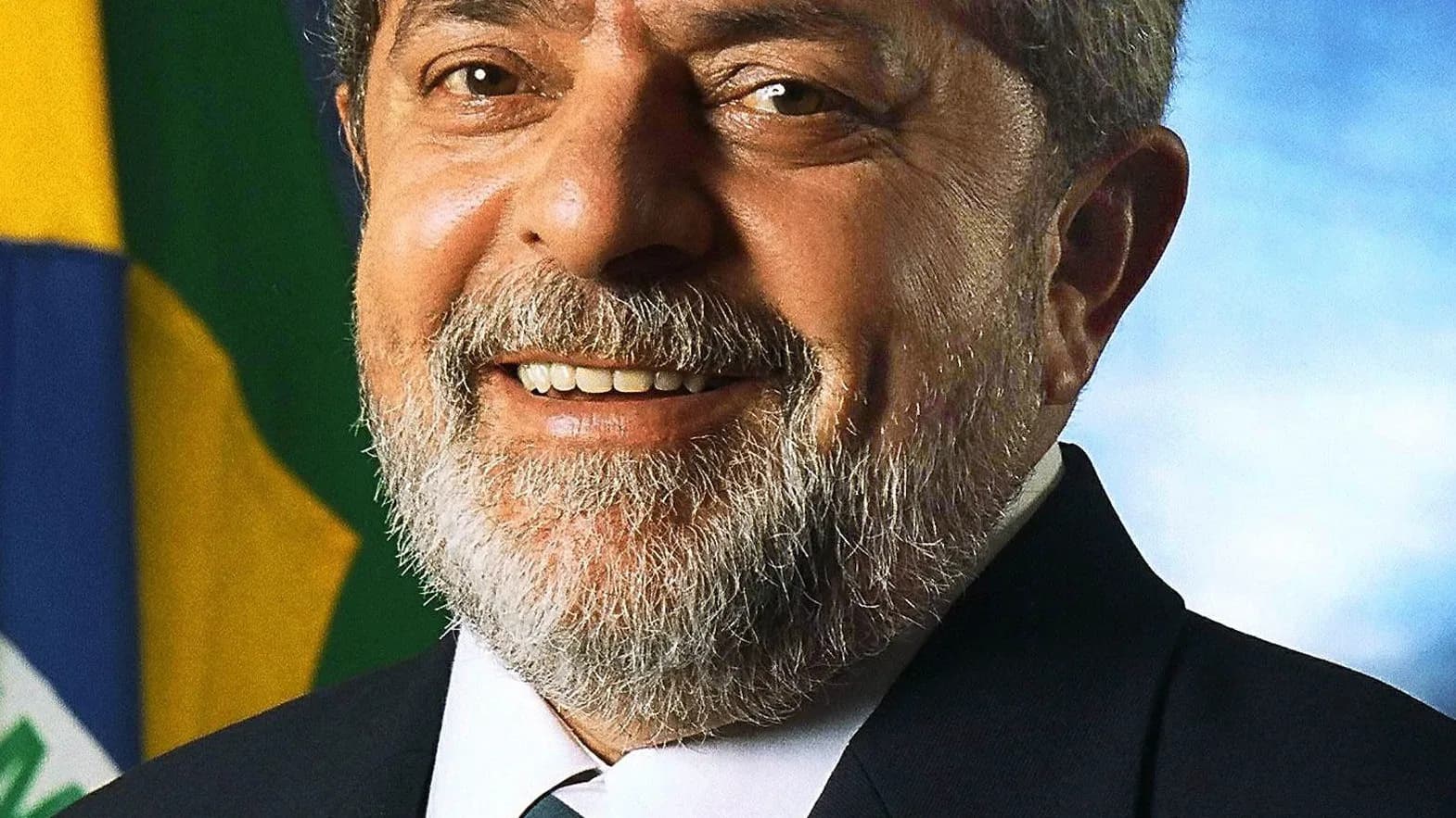Retrato oficial de Lula sorrindo, de terno escuro, com a bandeira do Brasil ao fundo